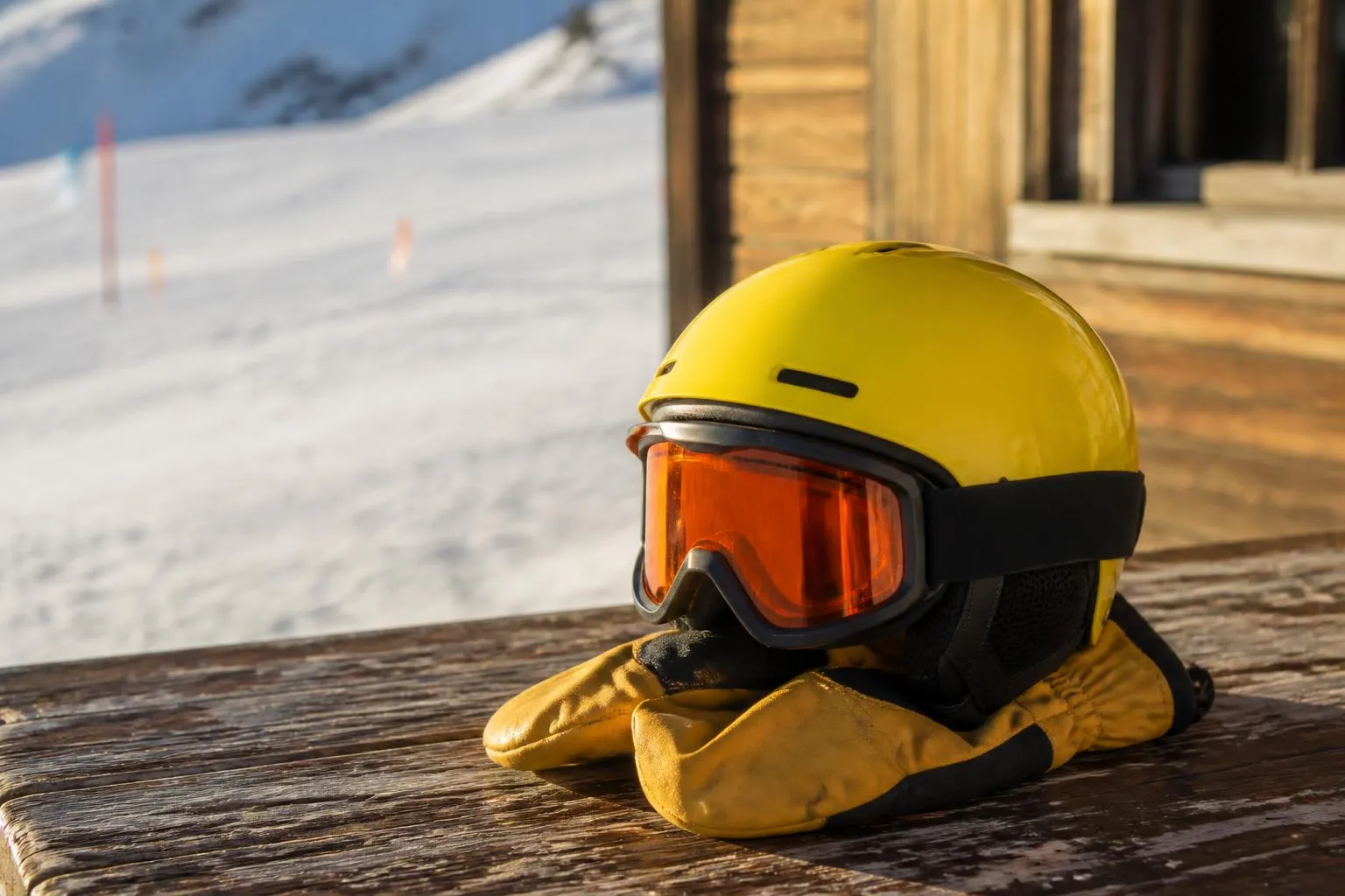 Un casque de ski d'enfant et un masque posés sur une paire de moufles, au bord d'une piste enneigée.
