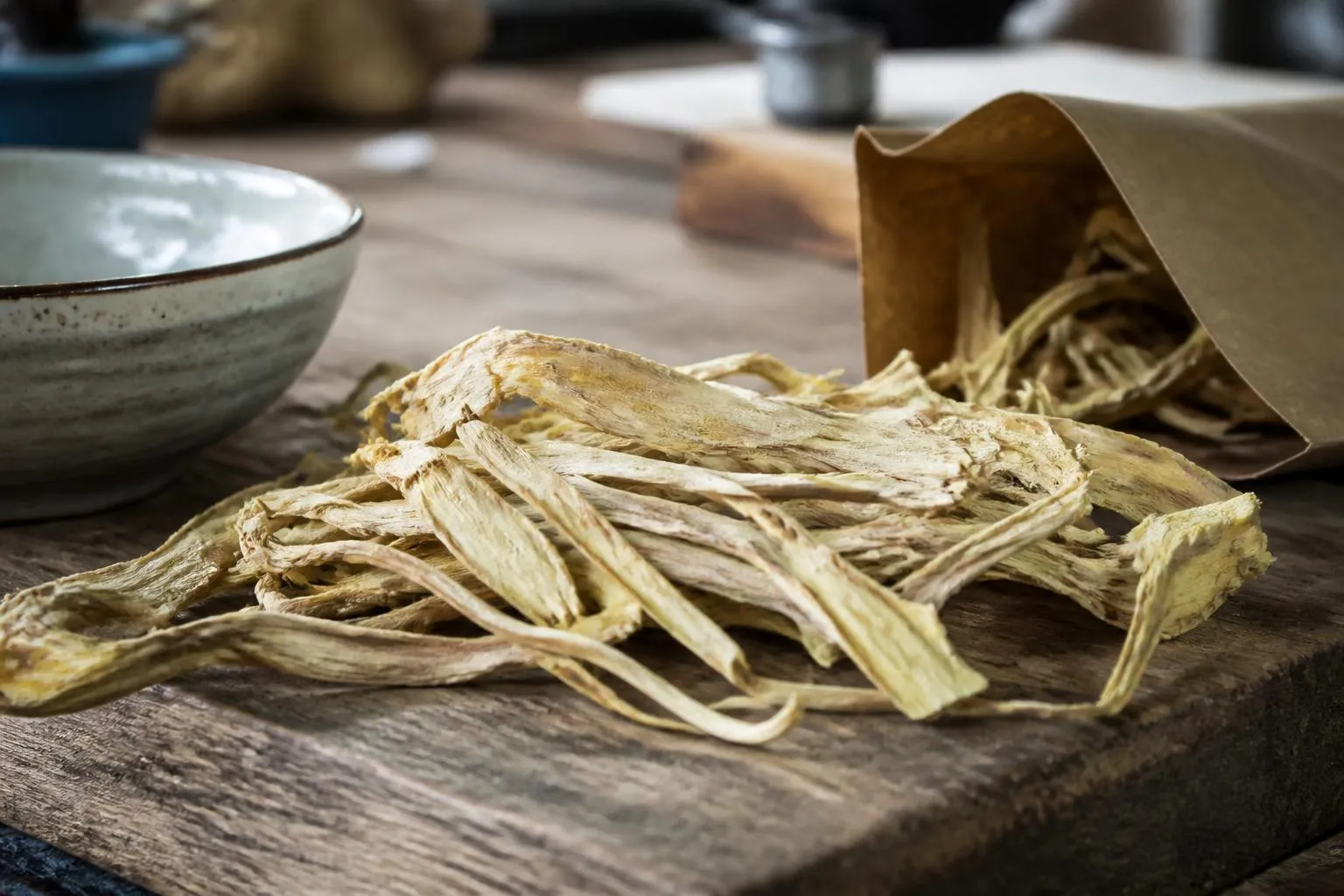 Lanières de racine d'astragale séchée, jaune pâle, posées en tas sur une planche de bois