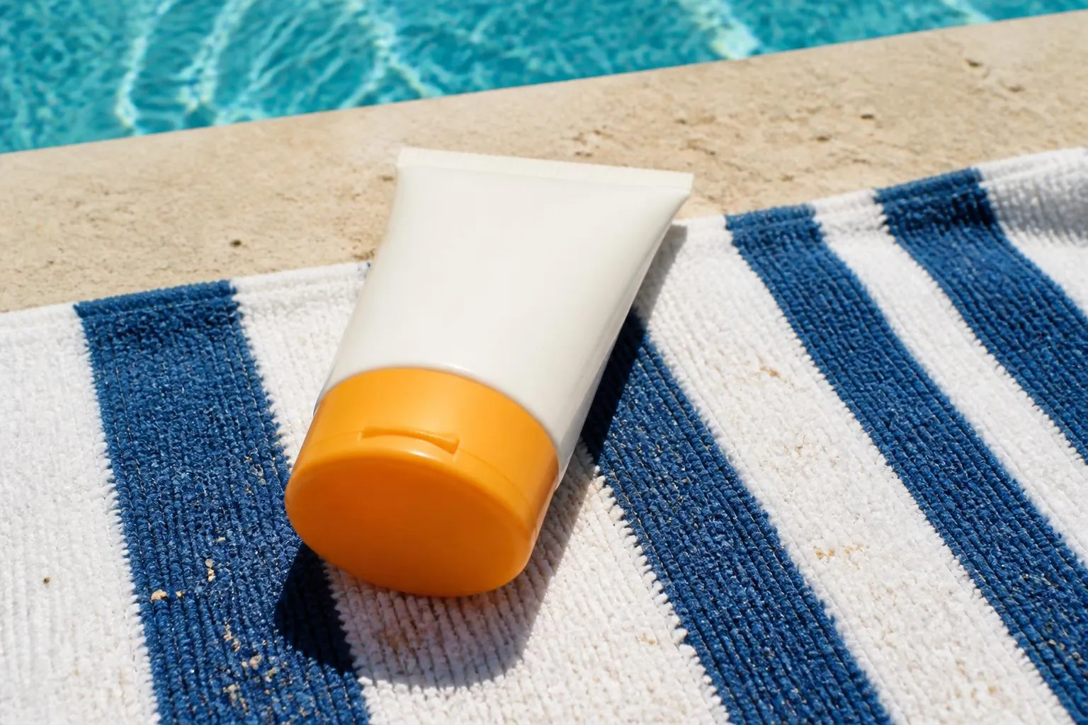Un flacon de crème solaire posé sur une serviette au bord d'une piscine, l'étiquette tournée vers le haut