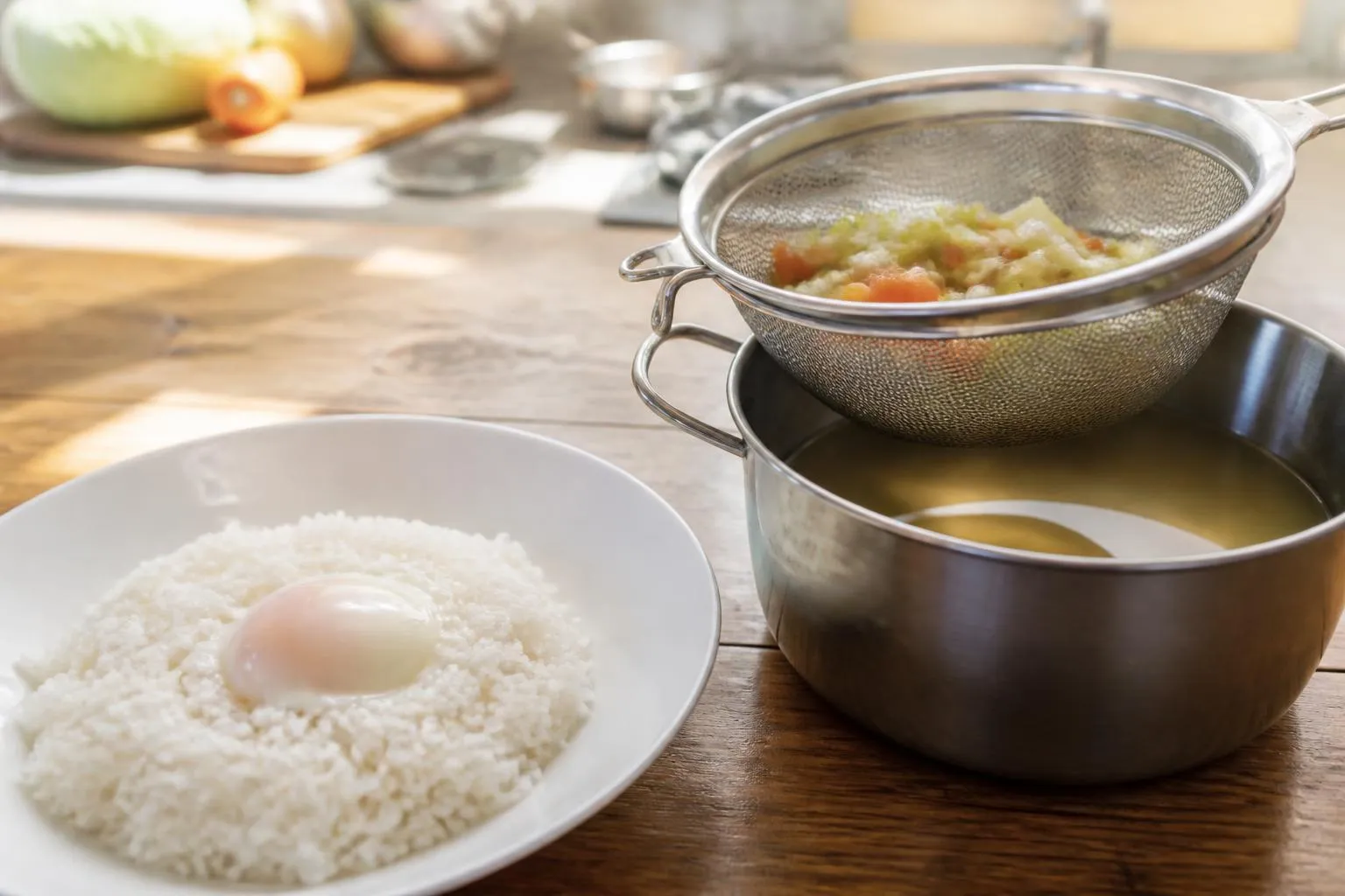 Une assiette de riz blanc et un œuf poché sur une table de cuisine, à côté d'un chinois et d'une casserole de bouillon filtré.