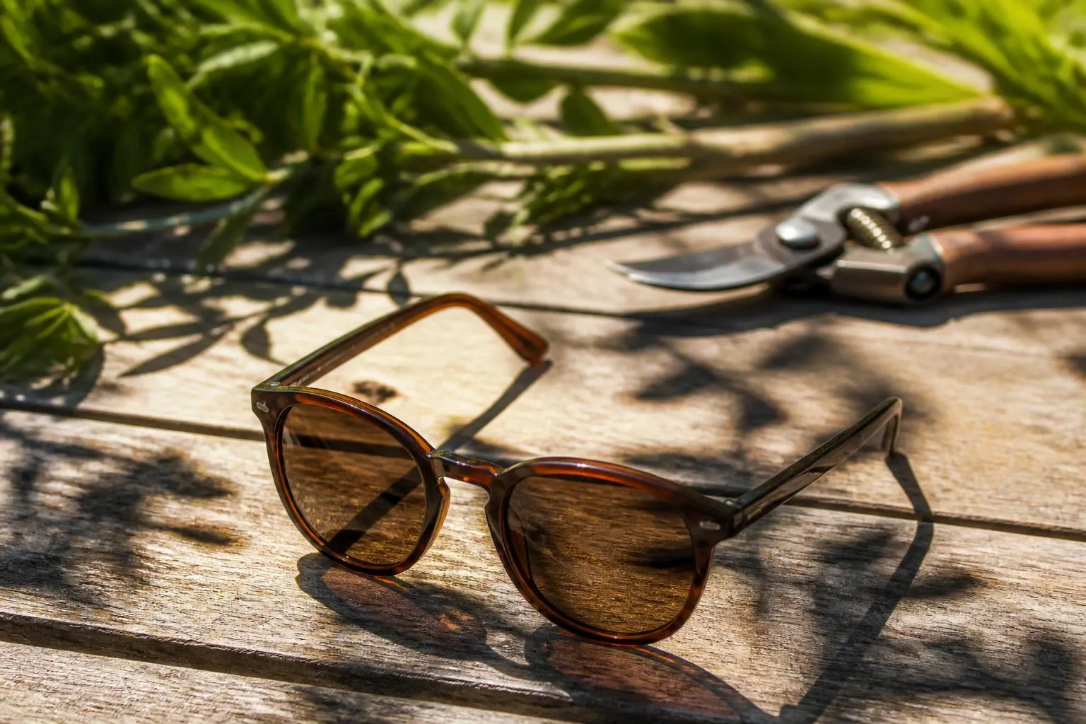 Une paire de lunettes de soleil posée branches ouvertes sur une table de jardin en plein soleil